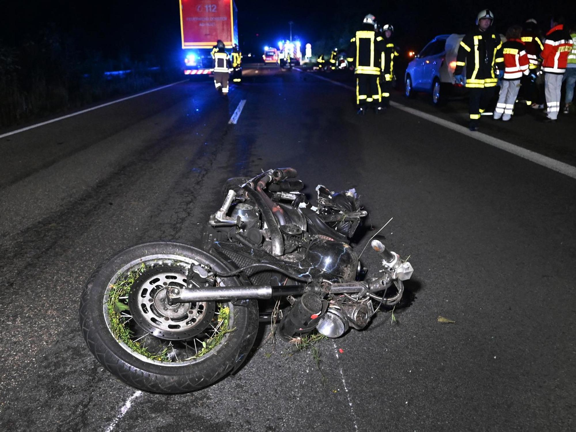 Ein zerstörtes Motorrad liegt auf der Autobahn, Rettungskräfte stehen dahinter.