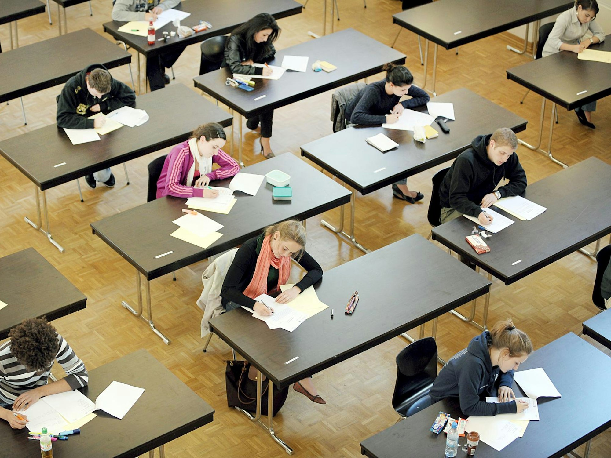 Junge Frauen und Männer sitzen bei einer Prüfung weit auseinander an Tischen.