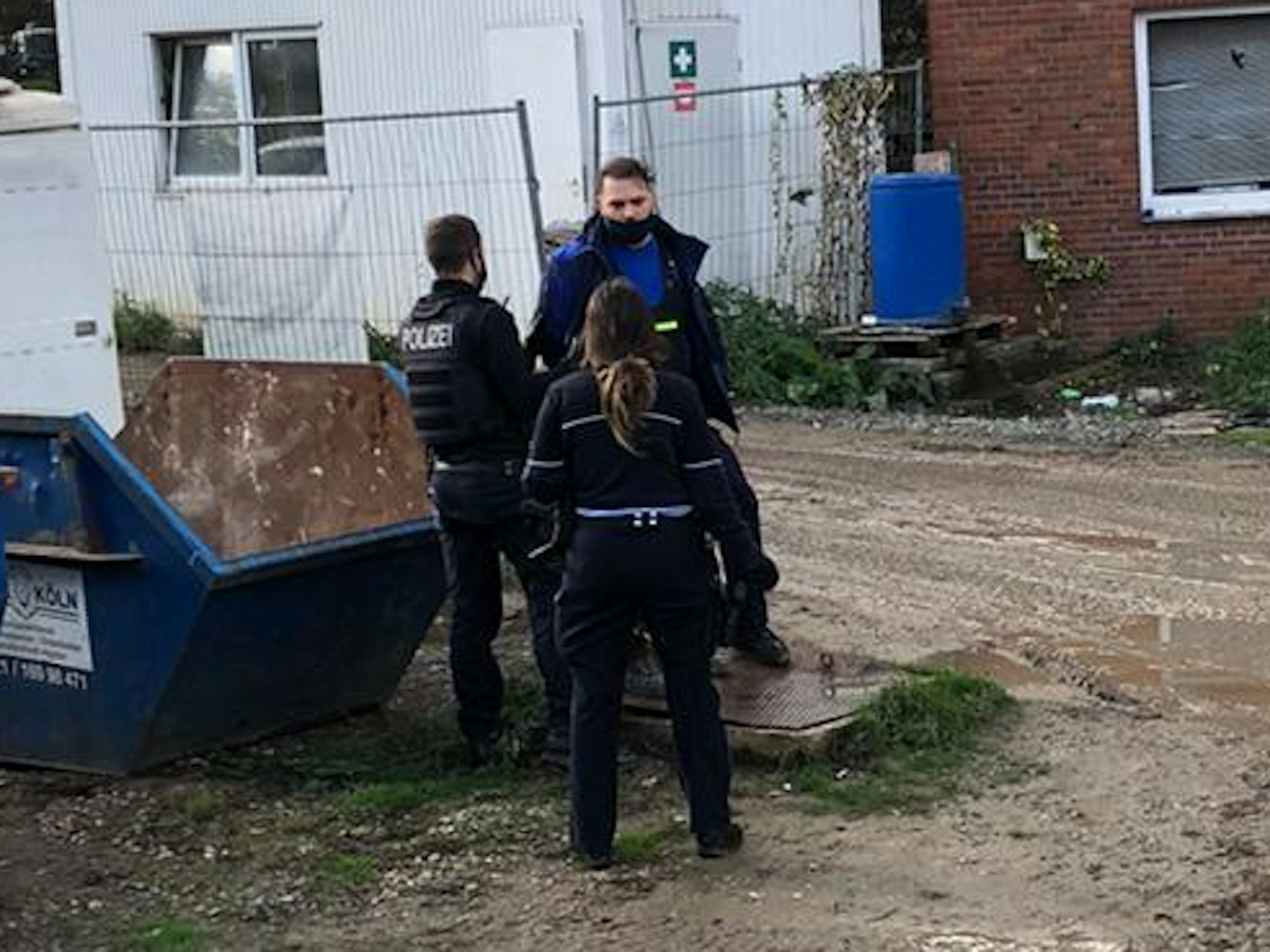 Yüksel Aker steht mit zwei Polizisten auf seinem Firmengelände in Köln.