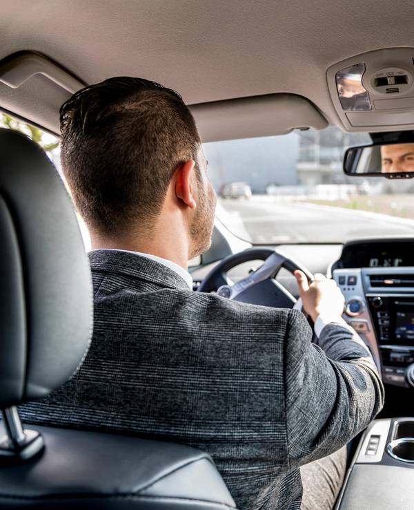 Ein Mann sitzt am Steuer eines Autos und schaut in den Rückspiegel.