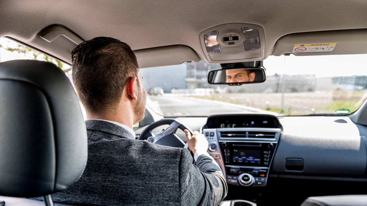 Ein Mann sitzt am Steuer eines Autos und schaut in den Rückspiegel.