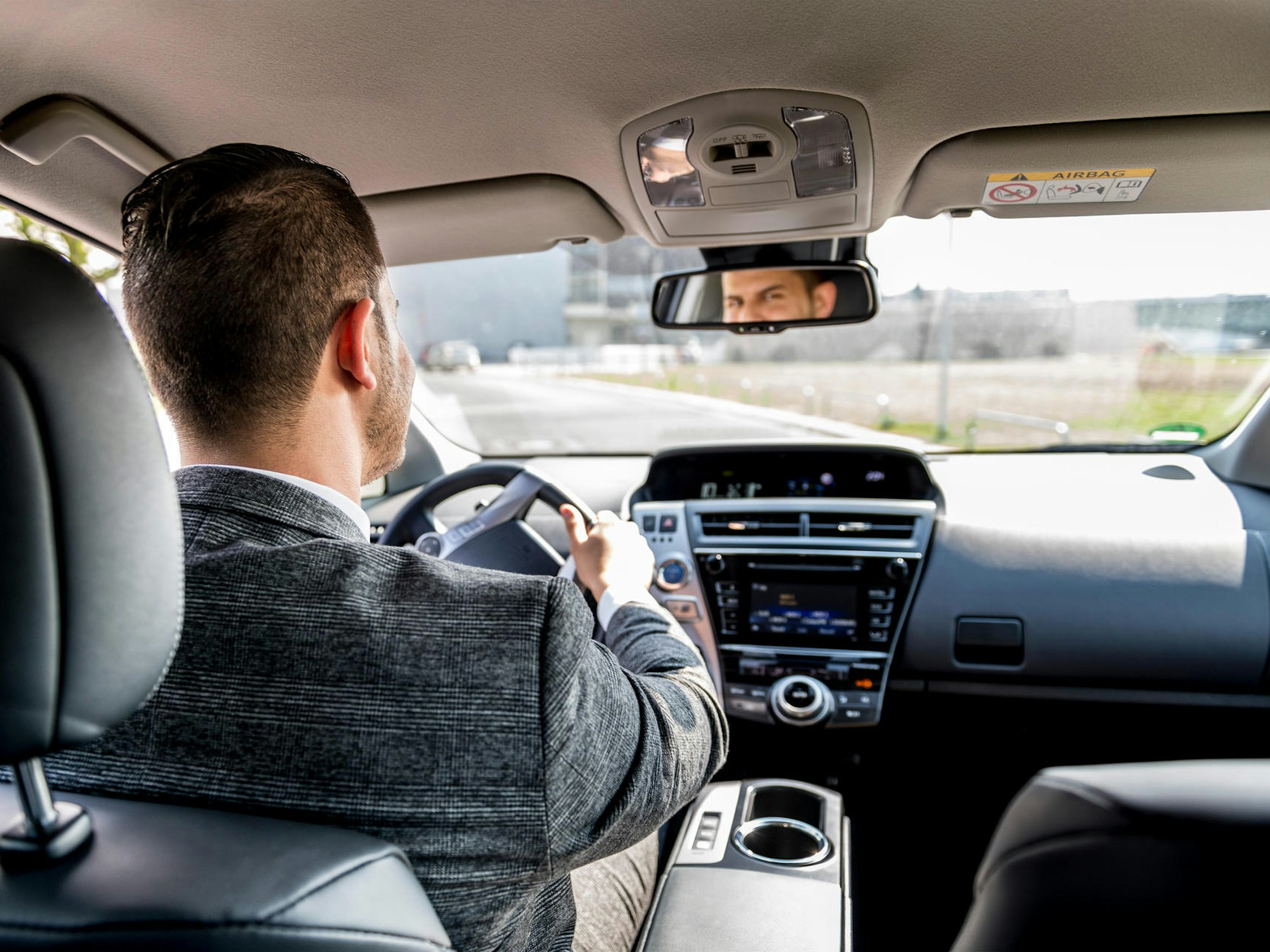 Ein Mann sitzt am Steuer eines Autos und schaut in den Rückspiegel.