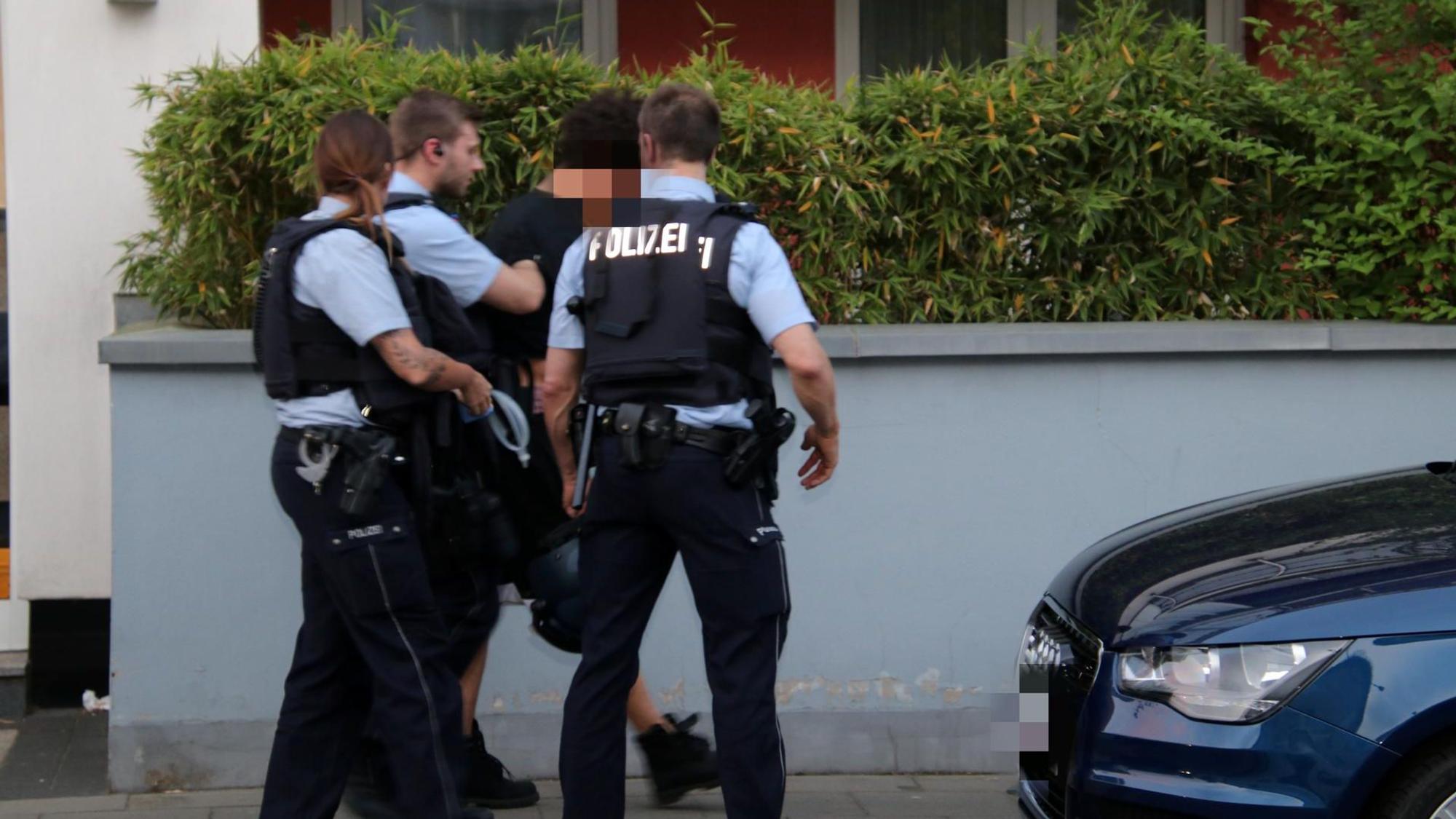 Zwei Polizisten und eine Polizistin führen auf der Straße einen Verdächtigen ab.