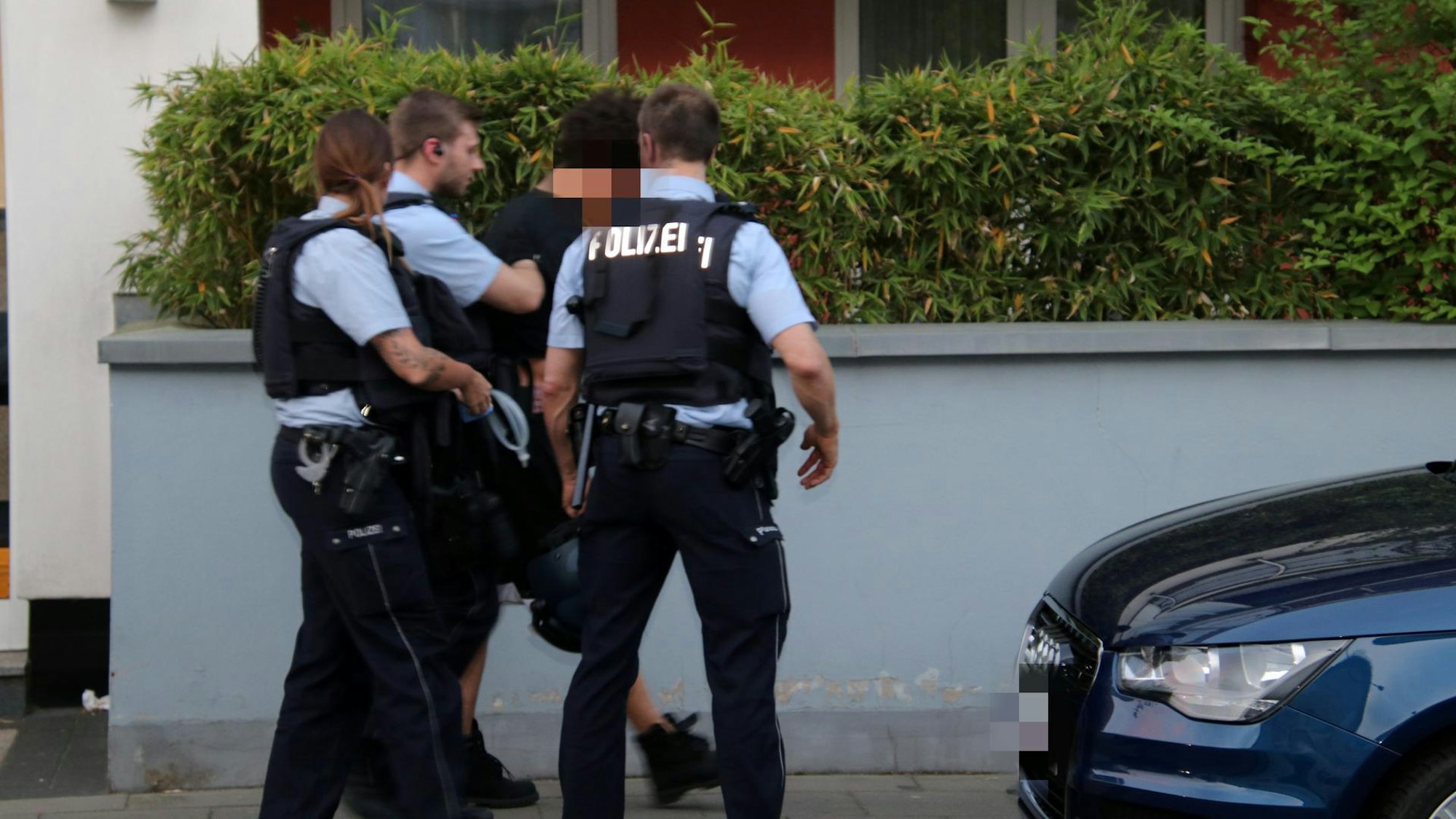 Zwei Polizisten und eine Polizistin führen auf der Straße einen Verdächtigen ab.