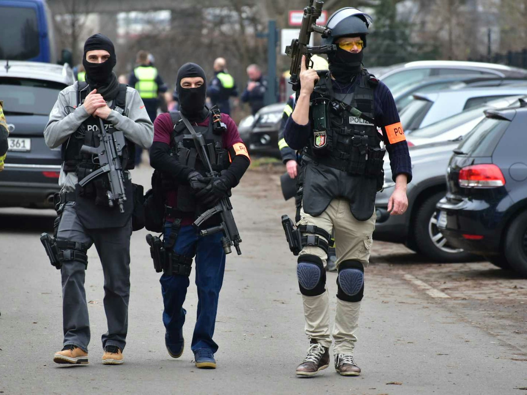 Drei vermummte und bewaffnete Kräfte eines Spezialeinsatzkommandos gehen über einen Parkplatz.