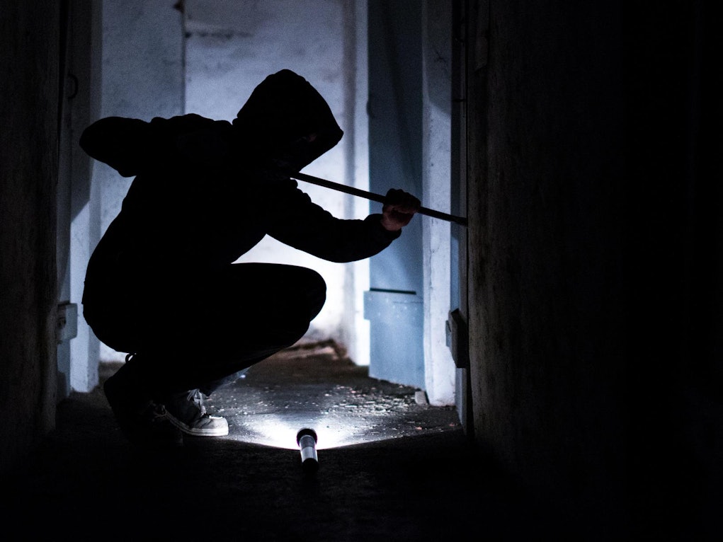 Eine Person macht sich mit einem Stemmeisen an der Tür zu schaffen.