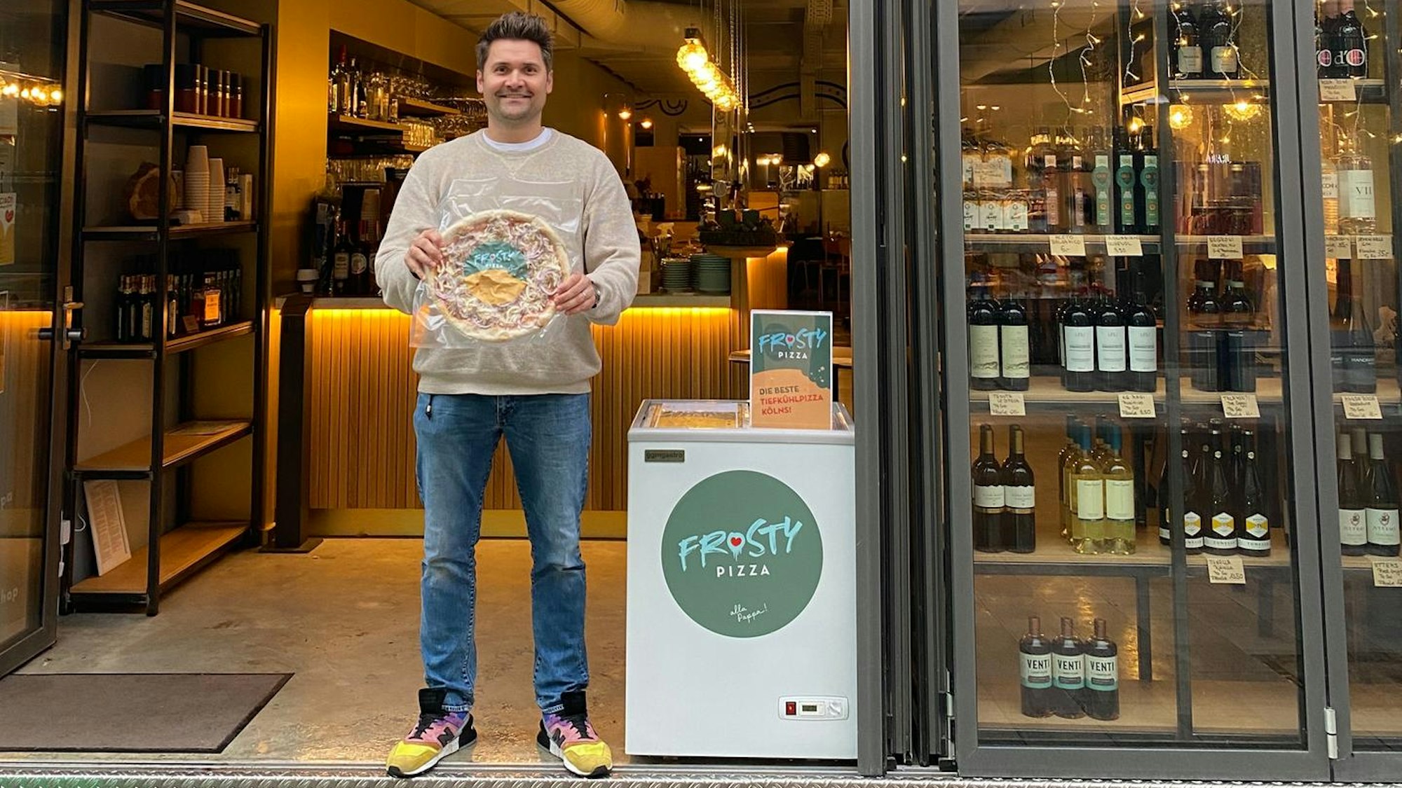 Robert Germer steht in der Tür seines Restaurants und hält eine verpackte Tiefkühlpizza in Händen.