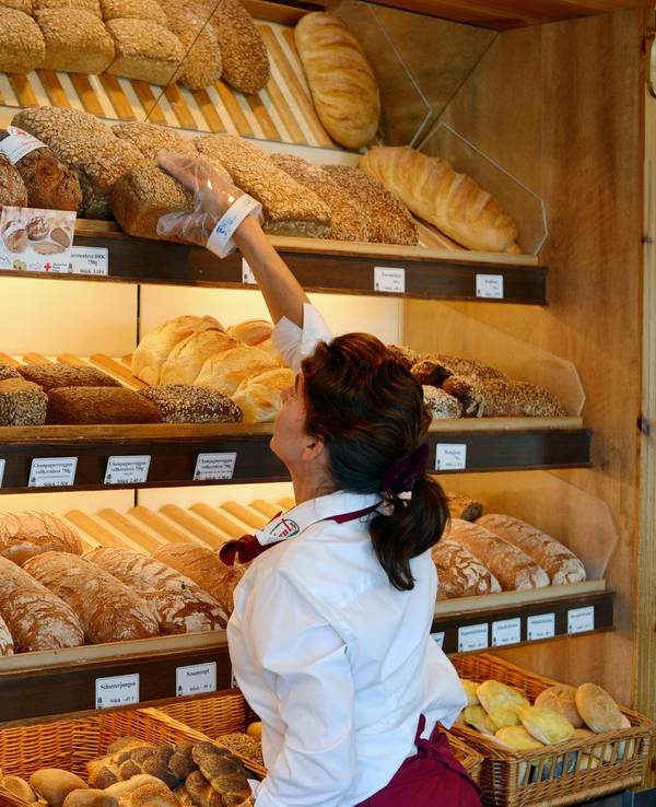 Bäckereifachverkäuferin vor Brot- und Brötchensortiment (undatiert).