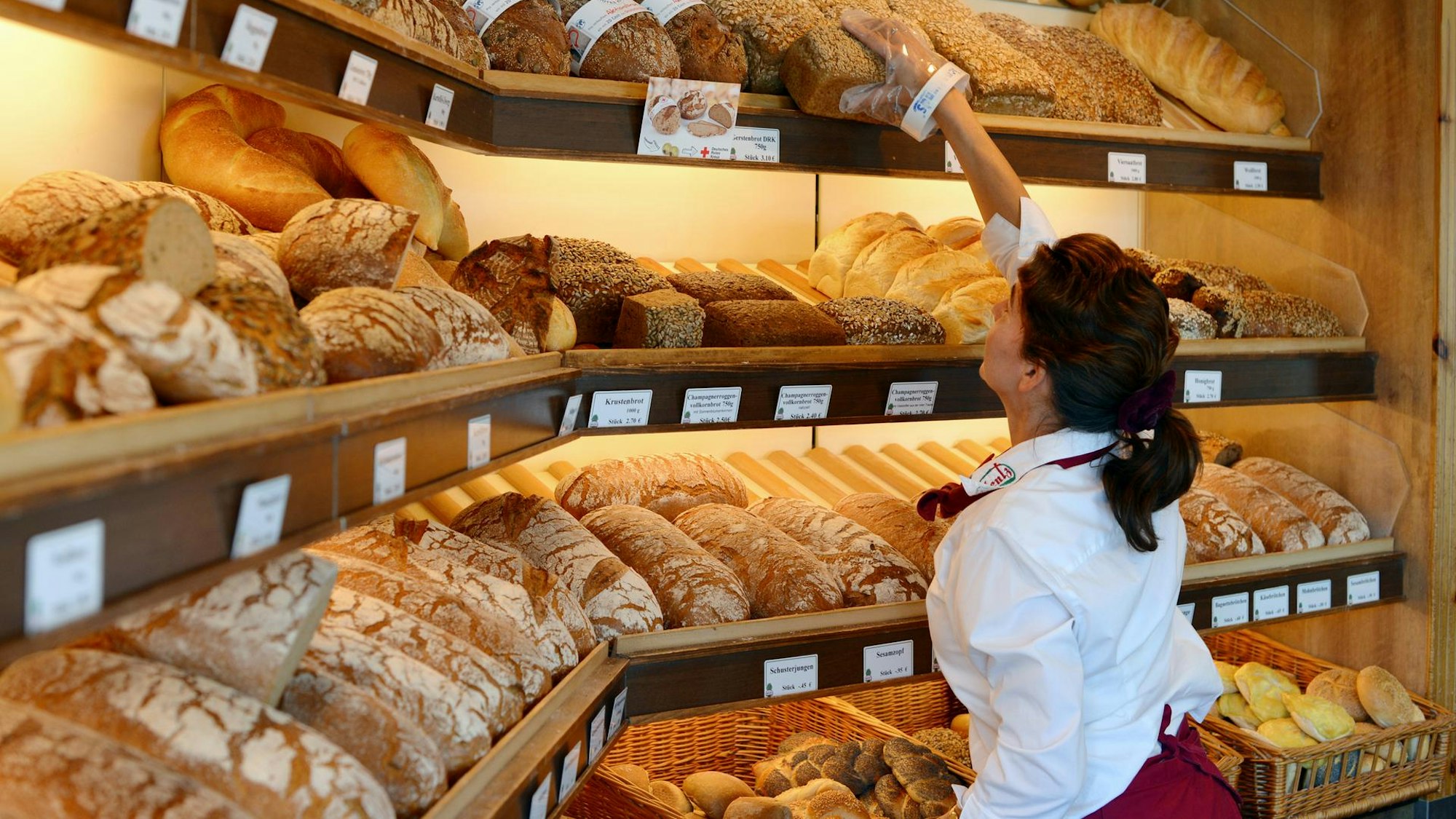 Bäckereifachverkäuferin vor Brot- und Brötchensortiment (undatiert).
