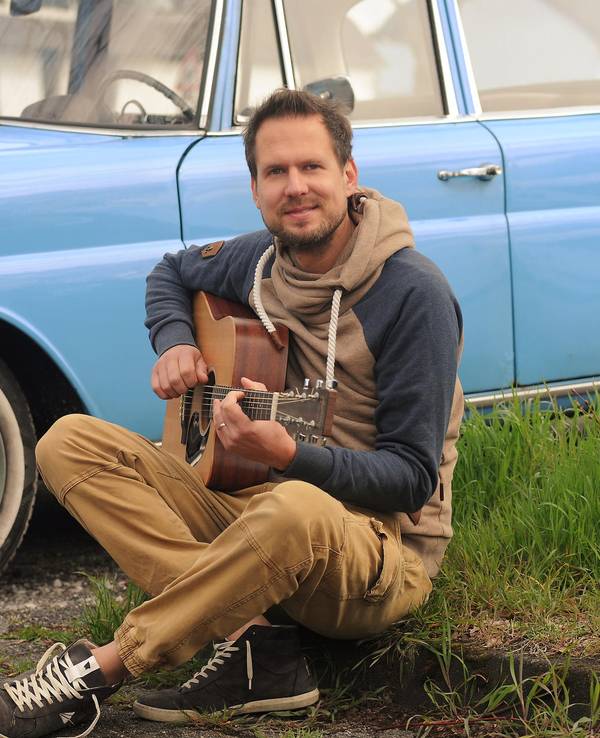 Mike Kremer von Miljö spielt sitzend Gitarre vor einem Auto