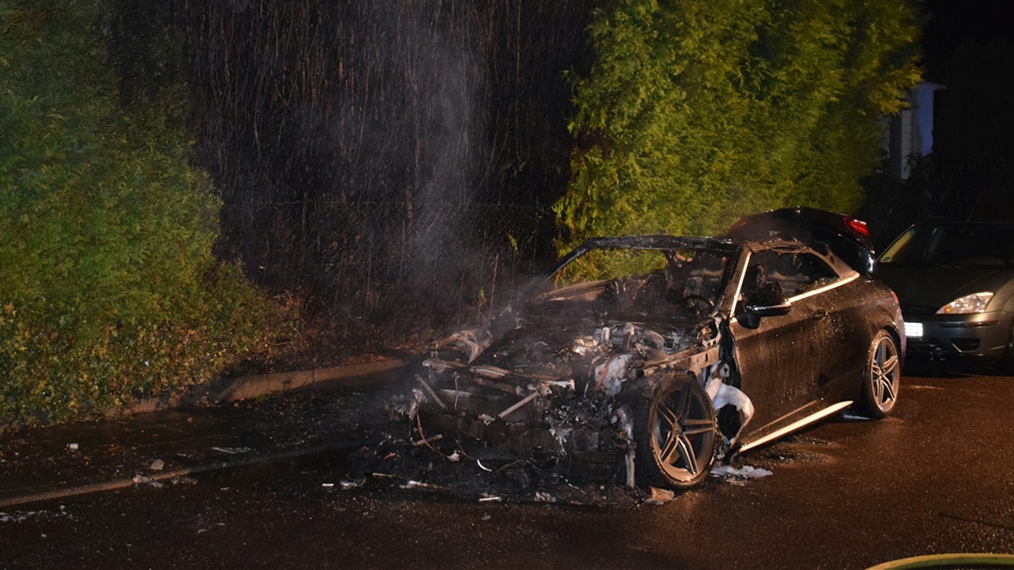 Ein ausgebrannter Mercedes steht an einer Straße.