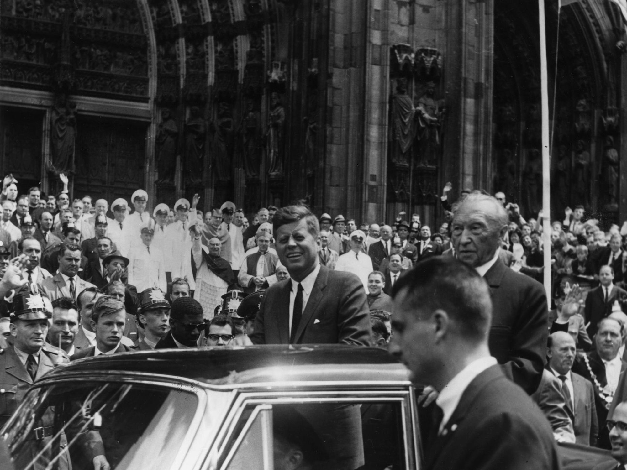John F. Kennedy wird vor dem Dom von einer riesigen Menschenmenge bejubelt. Begleitet wird der US-Präsident von Bundeskanzler Konrad Adenauer.