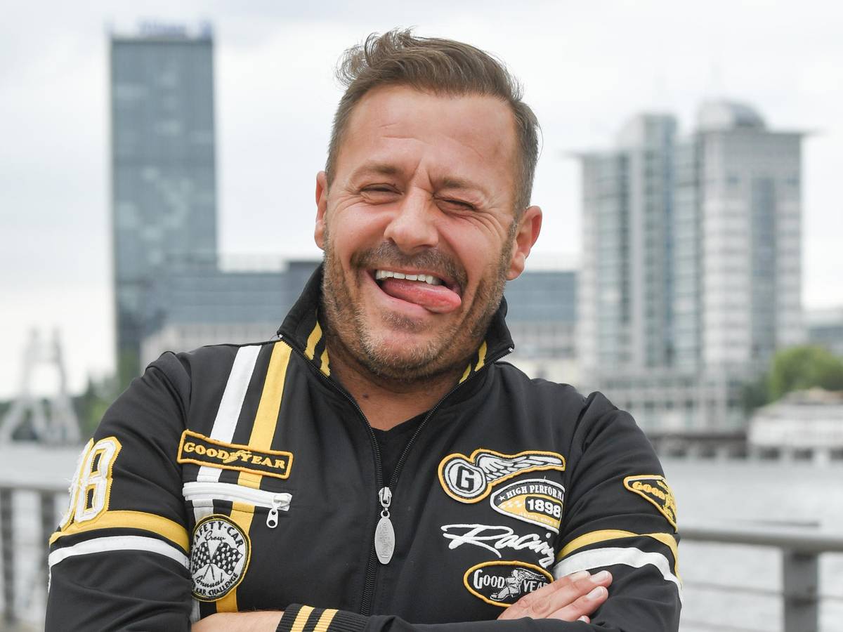 Willi Herren steht am Rhein und steckt die Zunge raus.