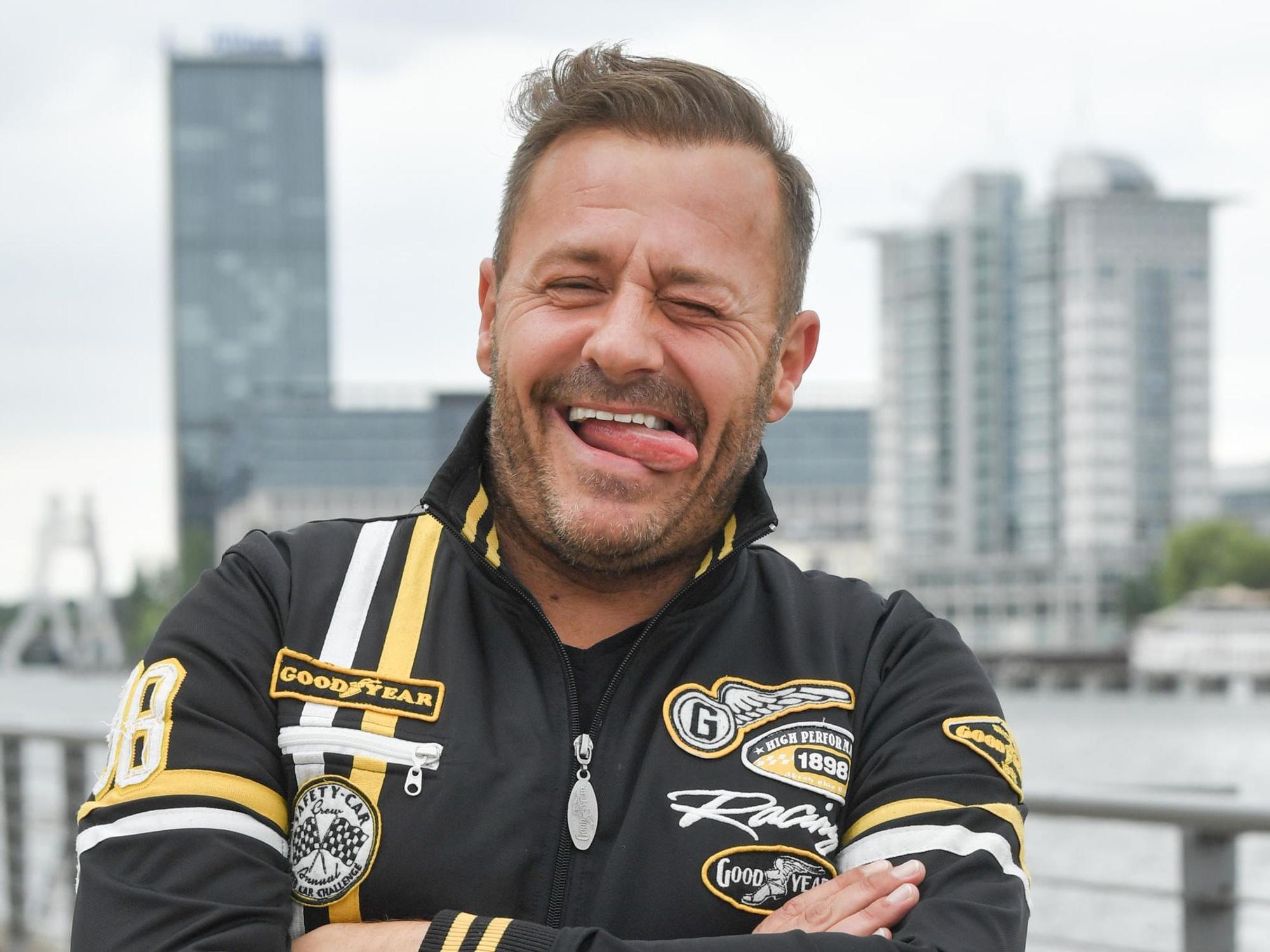 Willi Herren steht am Rhein und steckt die Zunge raus.