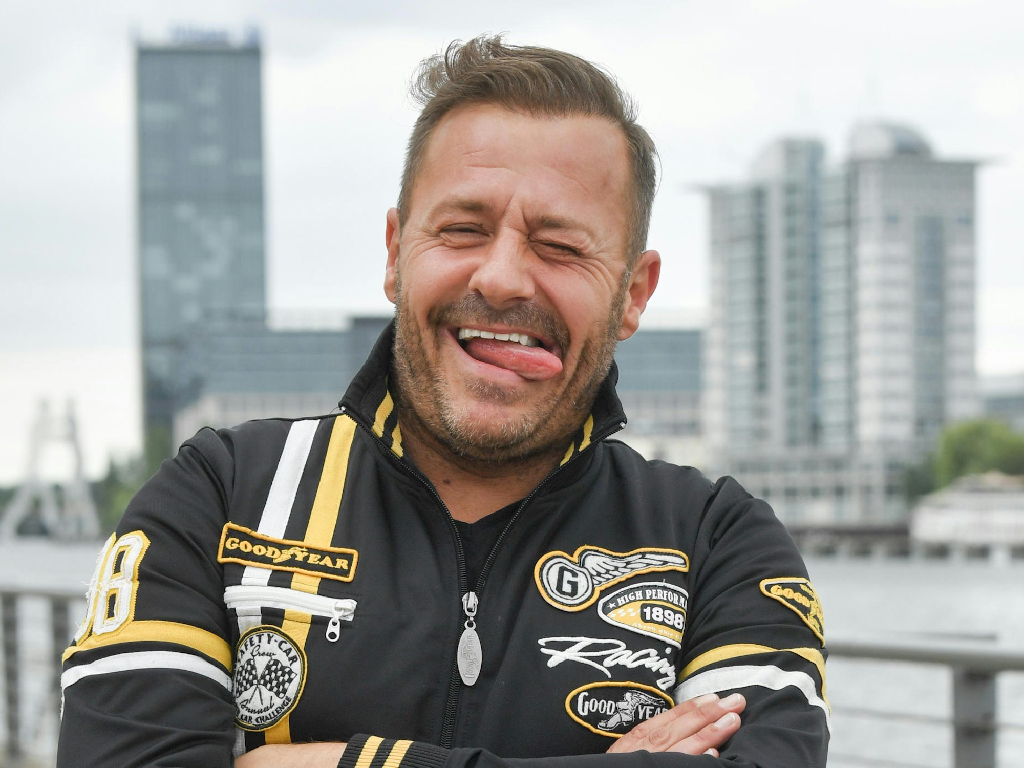 Willi Herren steht am Rhein und steckt die Zunge raus.