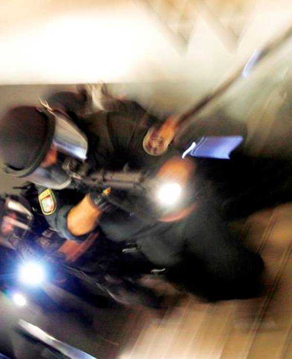 Vermummte und schwer bewaffnete Polizisten bewegen sich ein Treppe hoch.