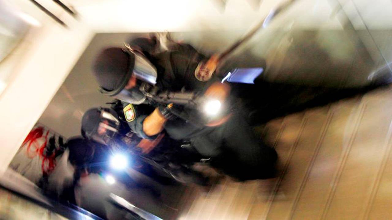 Vermummte und schwer bewaffnete Polizisten bewegen sich ein Treppe hoch.
