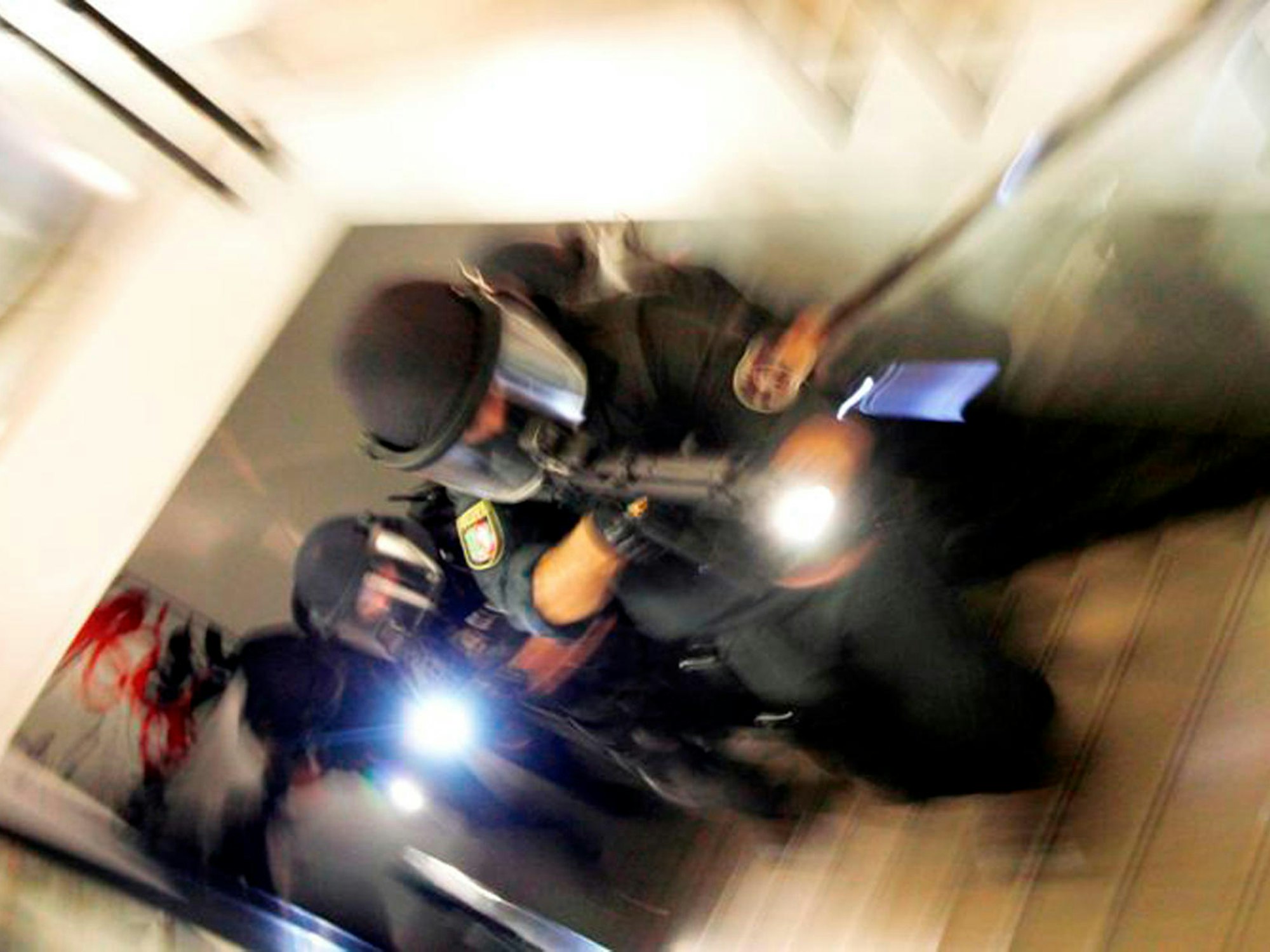 Vermummte und schwer bewaffnete Polizisten bewegen sich ein Treppe hoch.