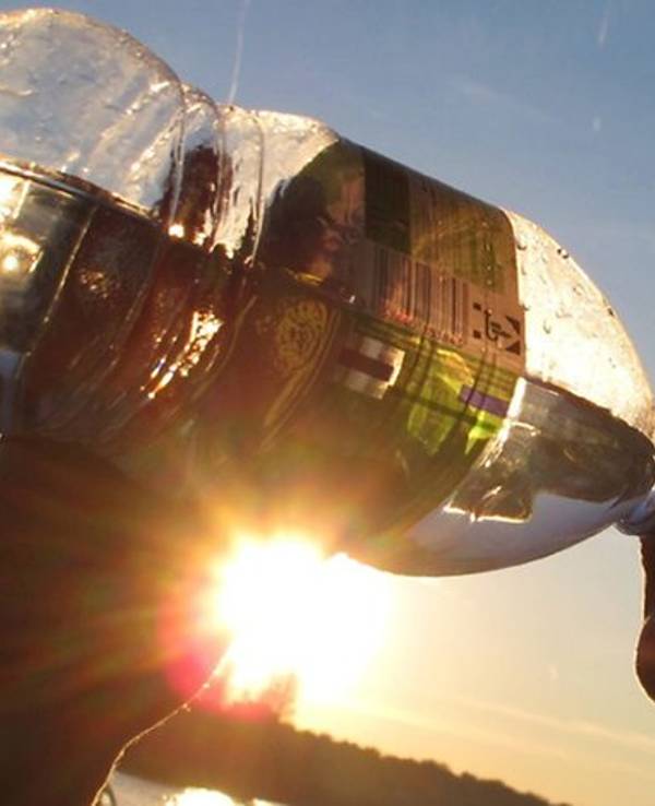 Das Symbolfoto zeigt einen Menschen, der aus einer Flasche trinkt. Im Hintergrund geht die Sonne unter.