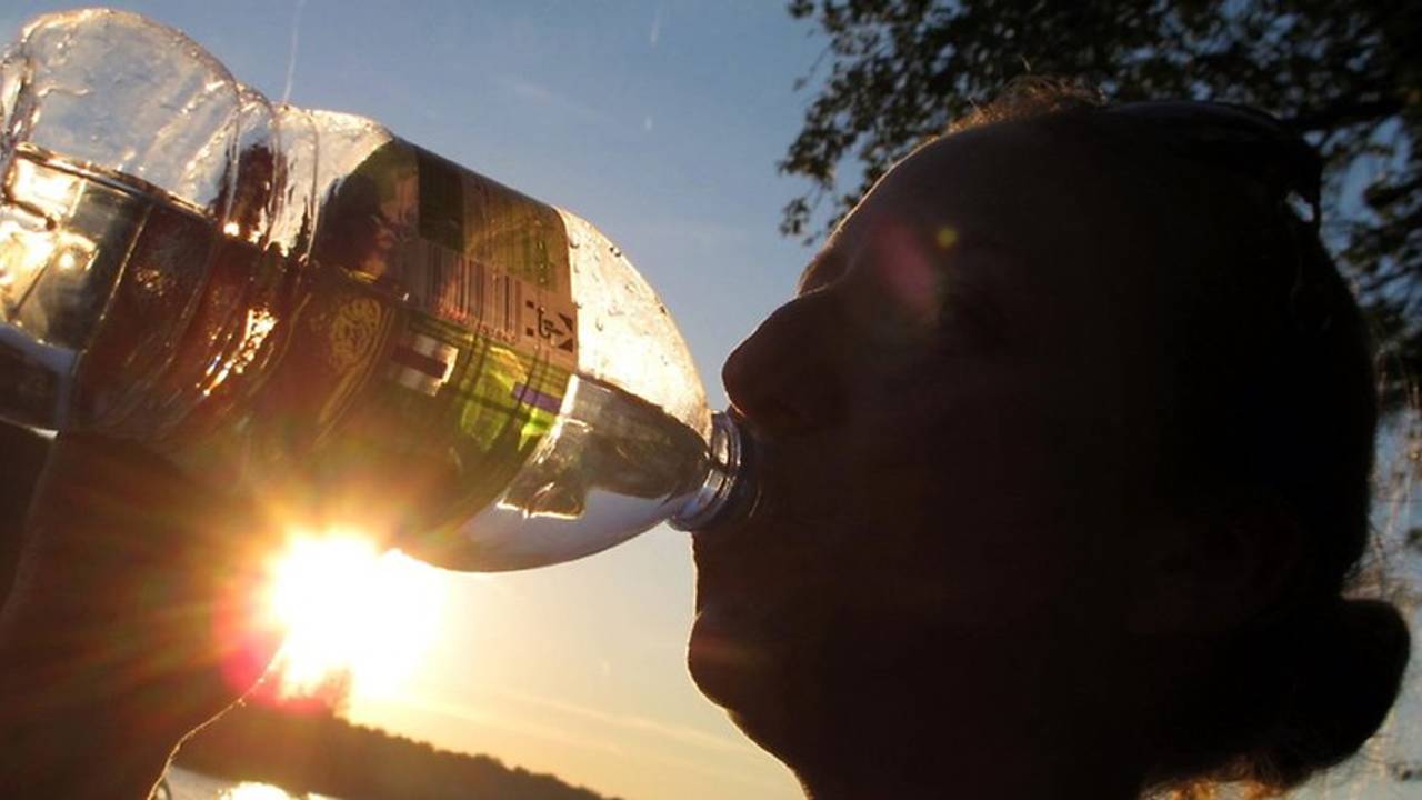 Das Symbolfoto zeigt einen Menschen, der aus einer Flasche trinkt. Im Hintergrund geht die Sonne unter.