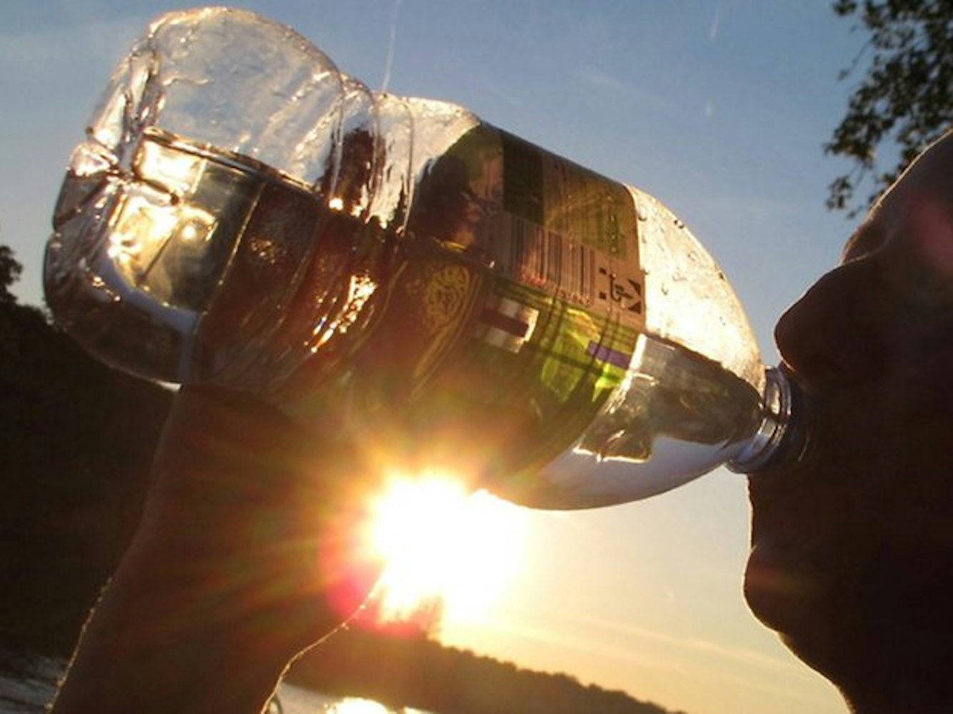 Das Symbolfoto zeigt einen Menschen, der aus einer Flasche trinkt. Im Hintergrund geht die Sonne unter.